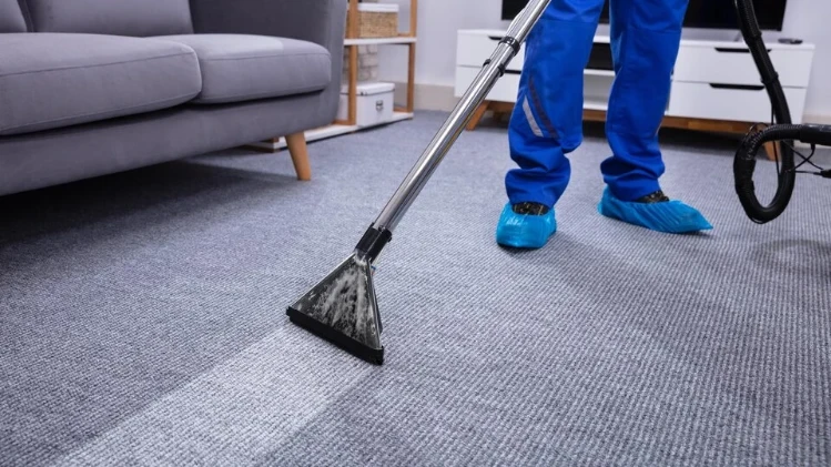 Technician using an extraction wand on gray carpet, wearing blue shoe covers.