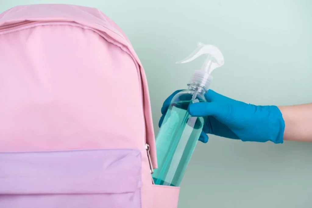 front view hand with surgical glove putting disinfectant bottle, book bag